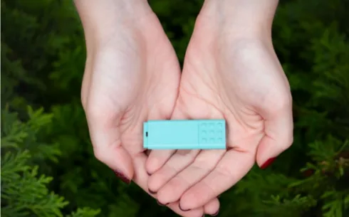 Dłonie trzymające miętową pamięć USB na tle zieleni